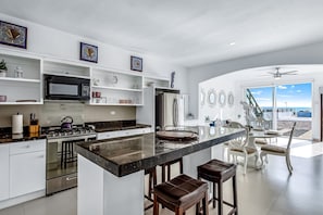 A modern kitchen with a central island, bar stools, and a view to the outside. - Dog-friendly Oceanfront Villa With Rooftop Patio, Pool Access, & Kitchen (Playas de Rosarito)