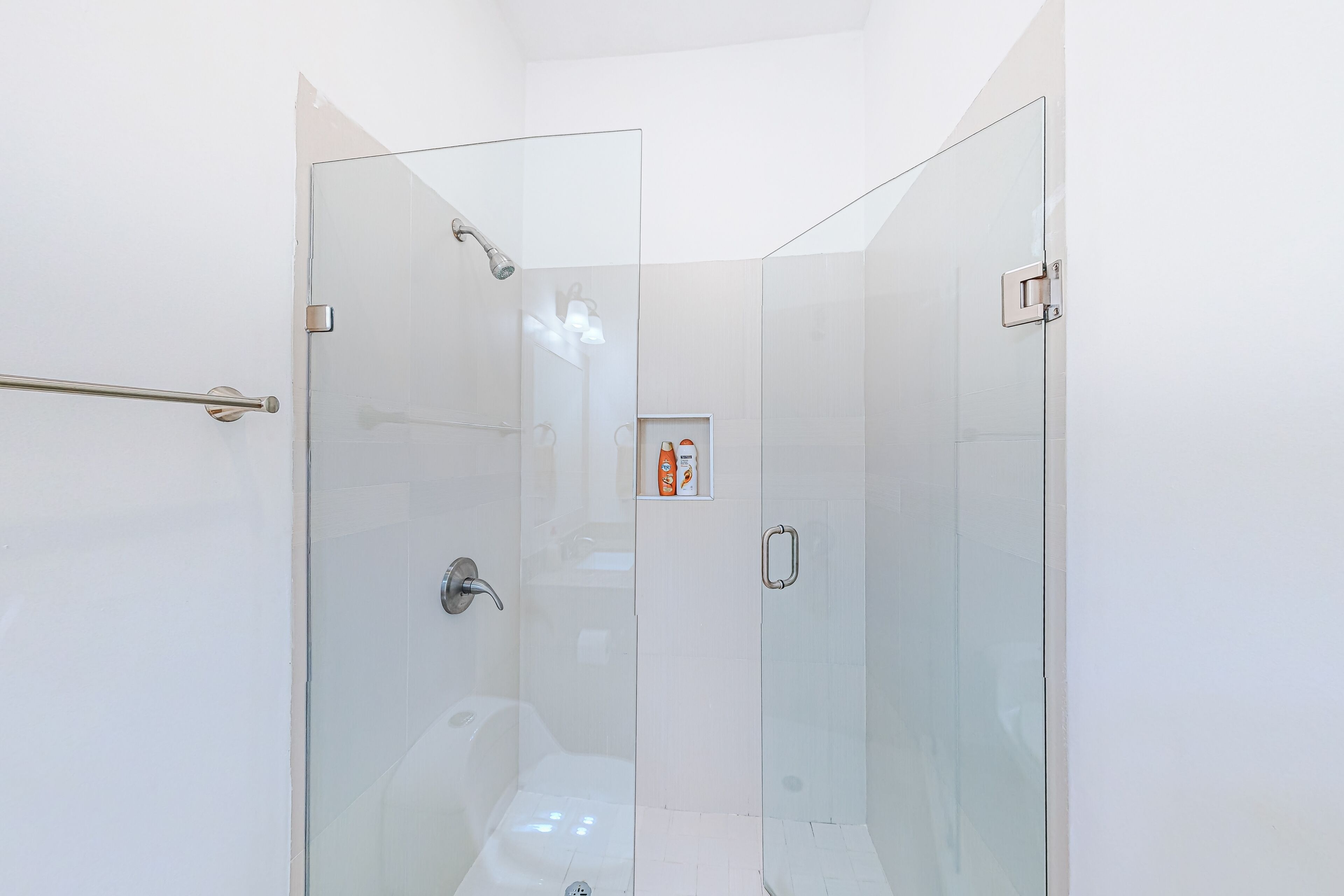 Een douche met glazen wanden, voorzien van een handgreep, een wandlamp en een klein plankje met toiletartikelen.