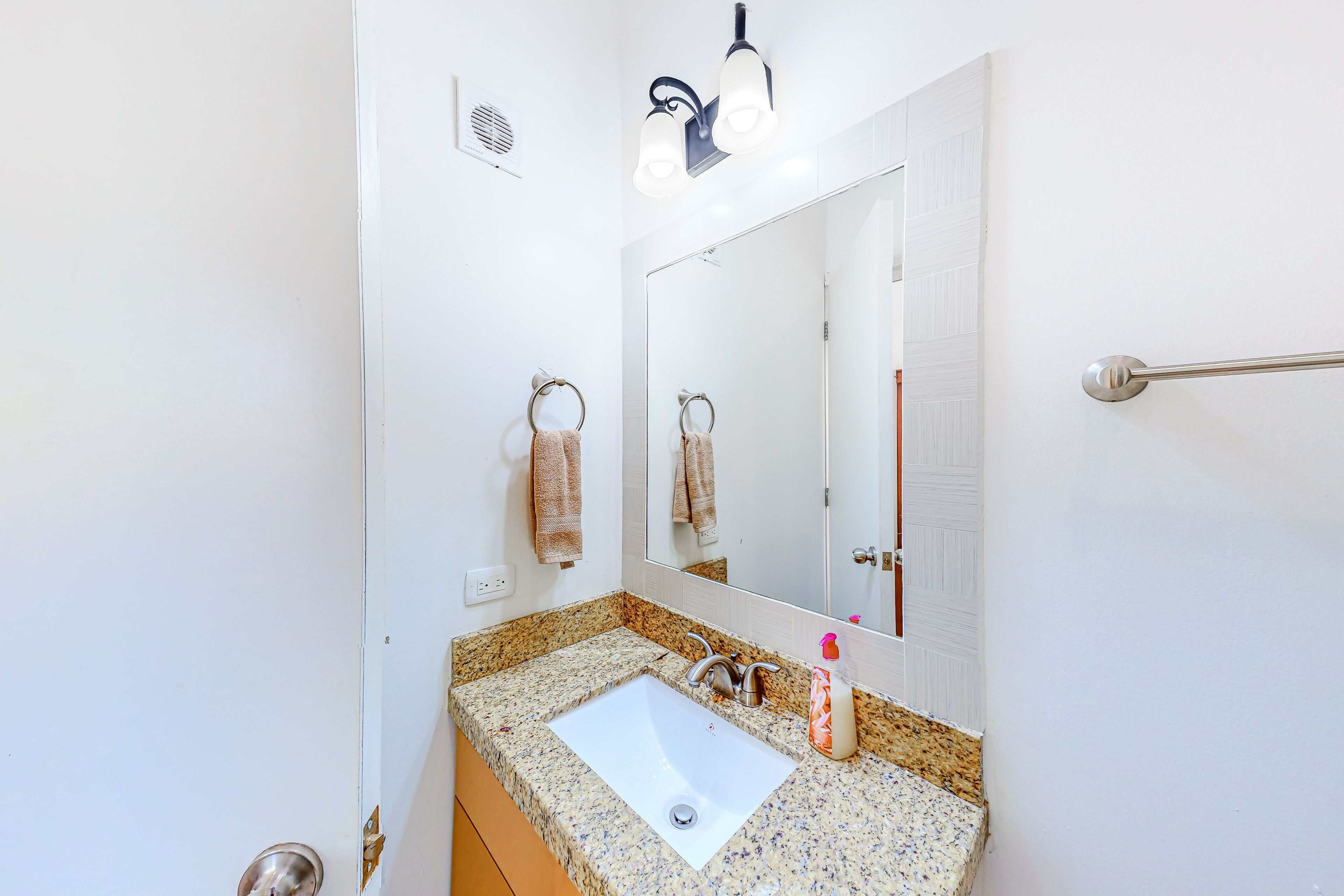 A bathroom with a white sink, granite countertop, and a mirror above it.