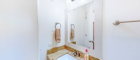 A bathroom with a white sink, granite countertop, and a mirror above it.