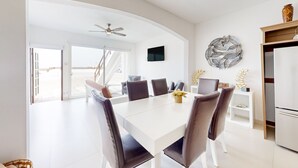 Un comedor moderno con una mesa blanca, sillas oscuras y un ventilador de techo.