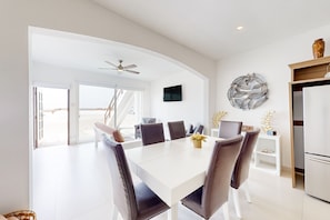 A modern dining area with a white table, brown chairs, a ceiling fan, and a TV mounted on the wall. - Dog-friendly Beachfront Retreat With Rooftop Deck, Pool, Hot Tub, & Kitchen (Playas de Rosarito)