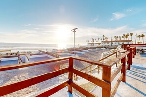 A beachside terrace with wooden railings, a pool, and a view of the ocean and palm trees. - Dog-friendly Beachfront Retreat With Rooftop Deck, Pool, Hot Tub, & Kitchen (Playas de Rosarito)