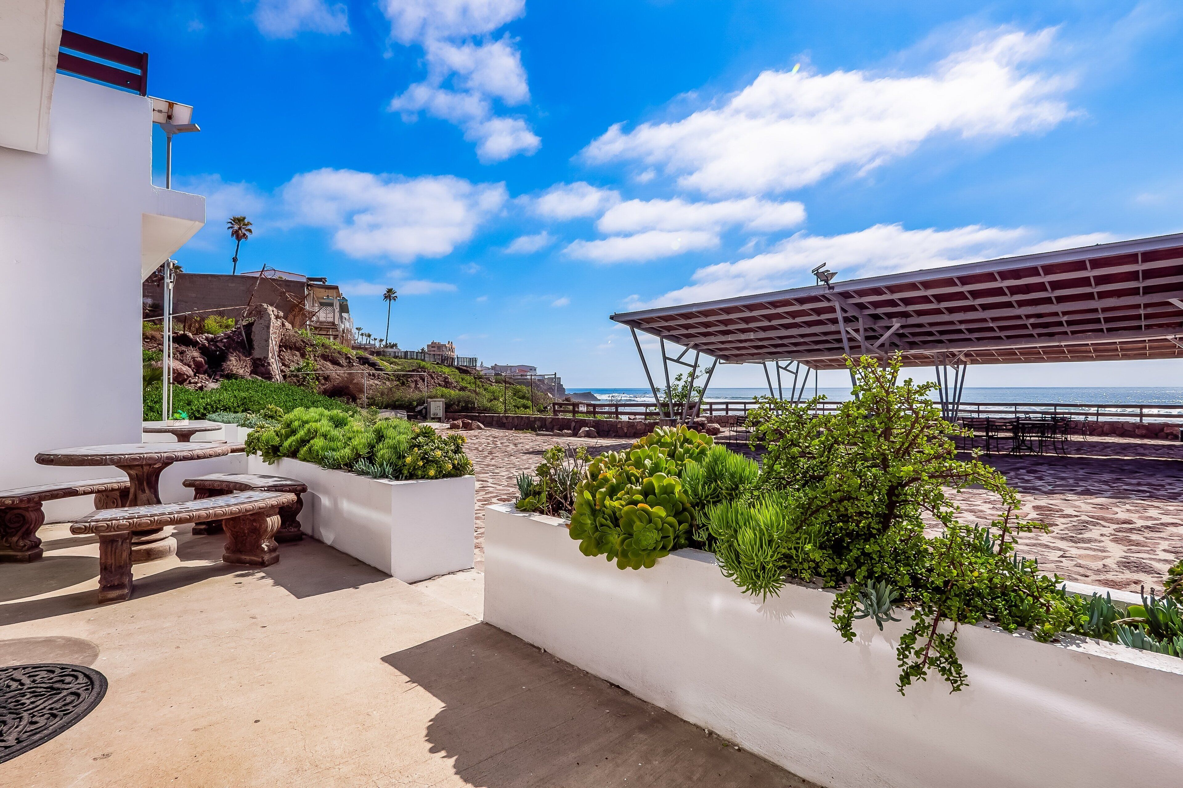 A rooftop terrace with outdoor seating, a pergola, and a view of the beach and ocean.