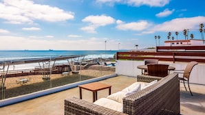 Terraza en la azotea con mobiliario de mimbre, una mesa de madera y vistas a la playa y al océano.