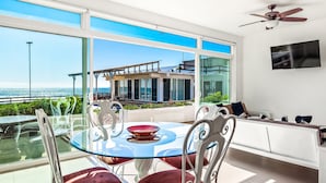 A modern room with a glass table and chairs, a ceiling fan, and a view of the sea. - Cheerful Dog-friendly Villa With Beach Views, Outdoor Pool, Private Patio, & AC (Playas de Rosarito)