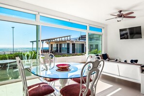 A modern room with a glass table and chairs, a ceiling fan, a TV, and a view of the sea. - Cheerful Dog-friendly Villa With Beach Views, Outdoor Pool, Private Patio, & AC (Playas de Rosarito)