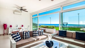 A modern living room with a sofa, coffee table, and large windows overlooking a coastal view. - Cheerful Dog-friendly Villa With Beach Views, Outdoor Pool, Private Patio, & AC (Playas de Rosarito)