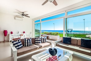 A modern living room with a sofa, coffee table, and large windows overlooking a coastal view. - Cheerful Dog-friendly Villa With Beach Views, Outdoor Pool, Private Patio, & AC (Playas de Rosarito)