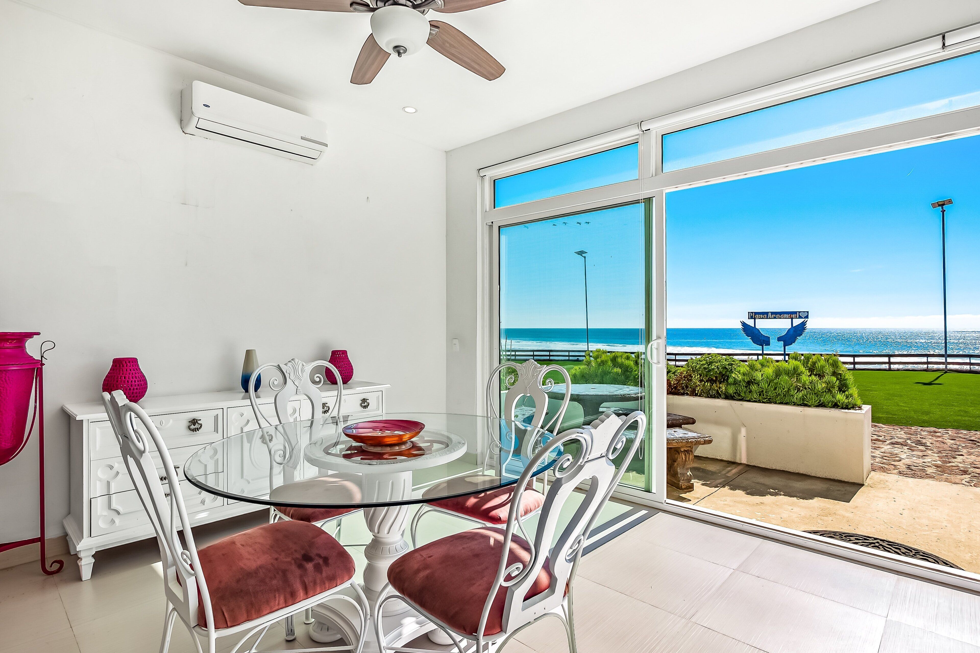 A dining area with a glass table and chairs, a white cabinet, and a view of the beach.