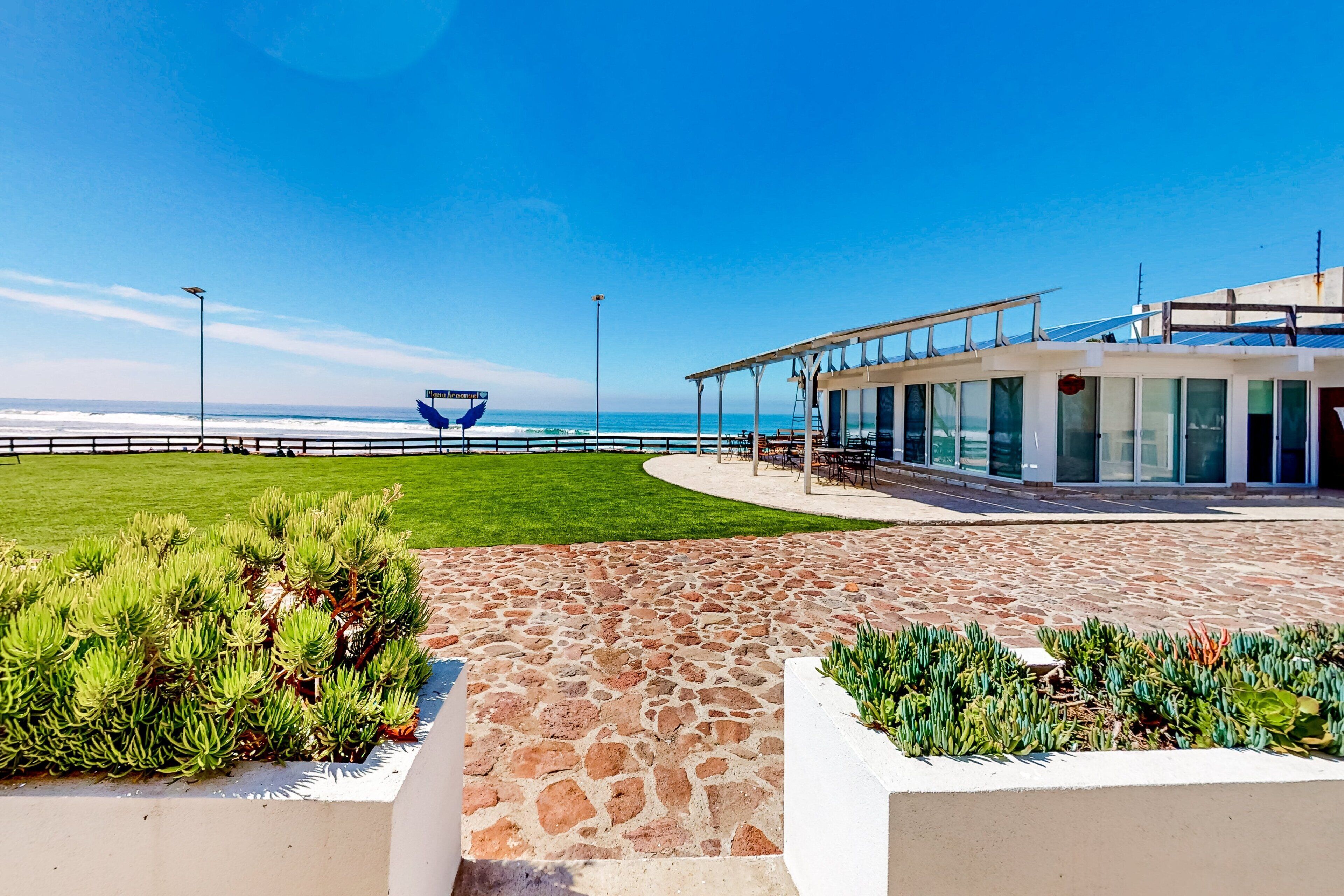 Un paseo marítimo con sendero de piedra, jardines verdes y un edificio moderno con amplias ventanas.