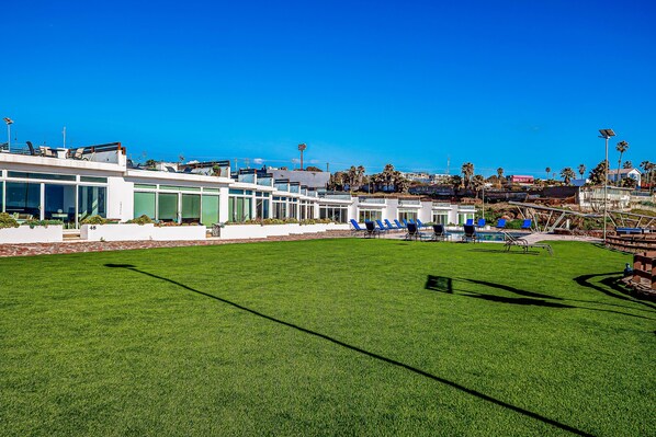 A modern building with a pool area, including a well-maintained lawn and blue lounge chairs. - Cheerful Dog-friendly Villa With Beach Views, Outdoor Pool, Private Patio, & AC (Playas de Rosarito)