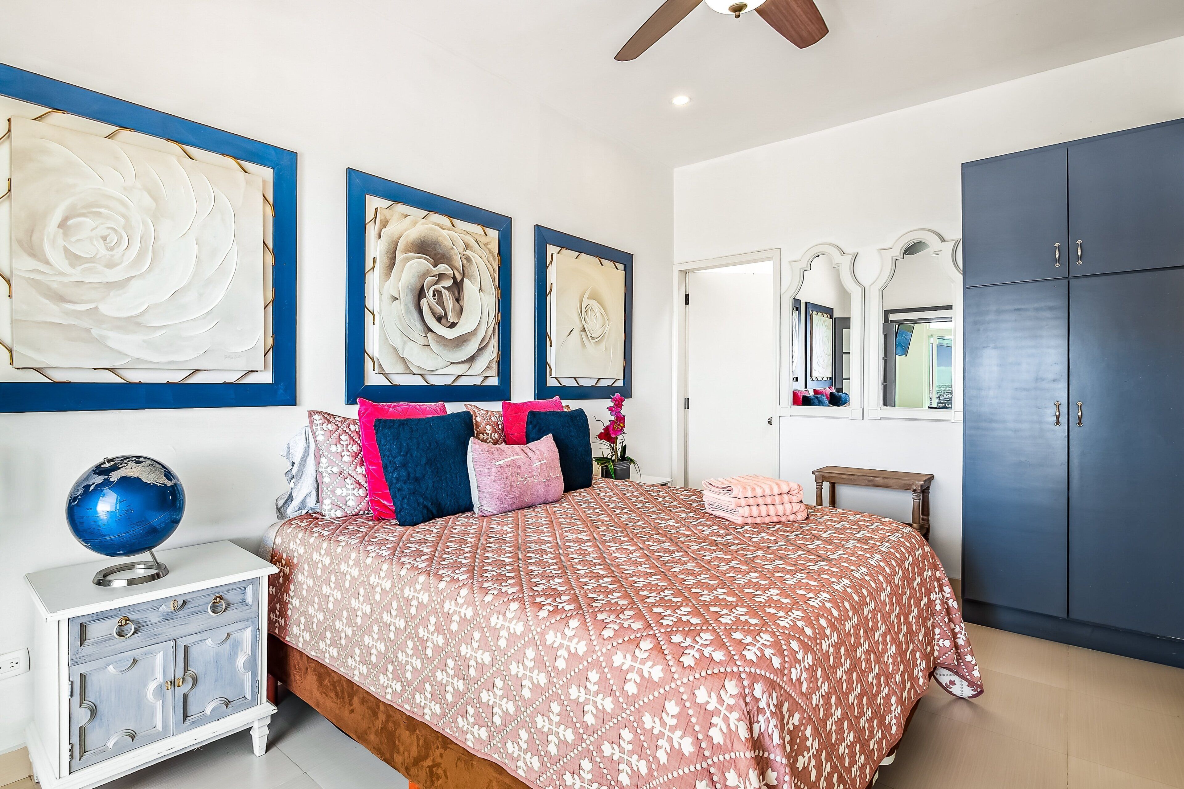 A bedroom with a bed, a nightstand, a wardrobe, and three wall-mounted artworks.