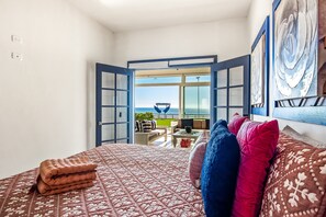 Quarto com cama, almofadas, vista para o exterior e porta que dá para uma varanda.