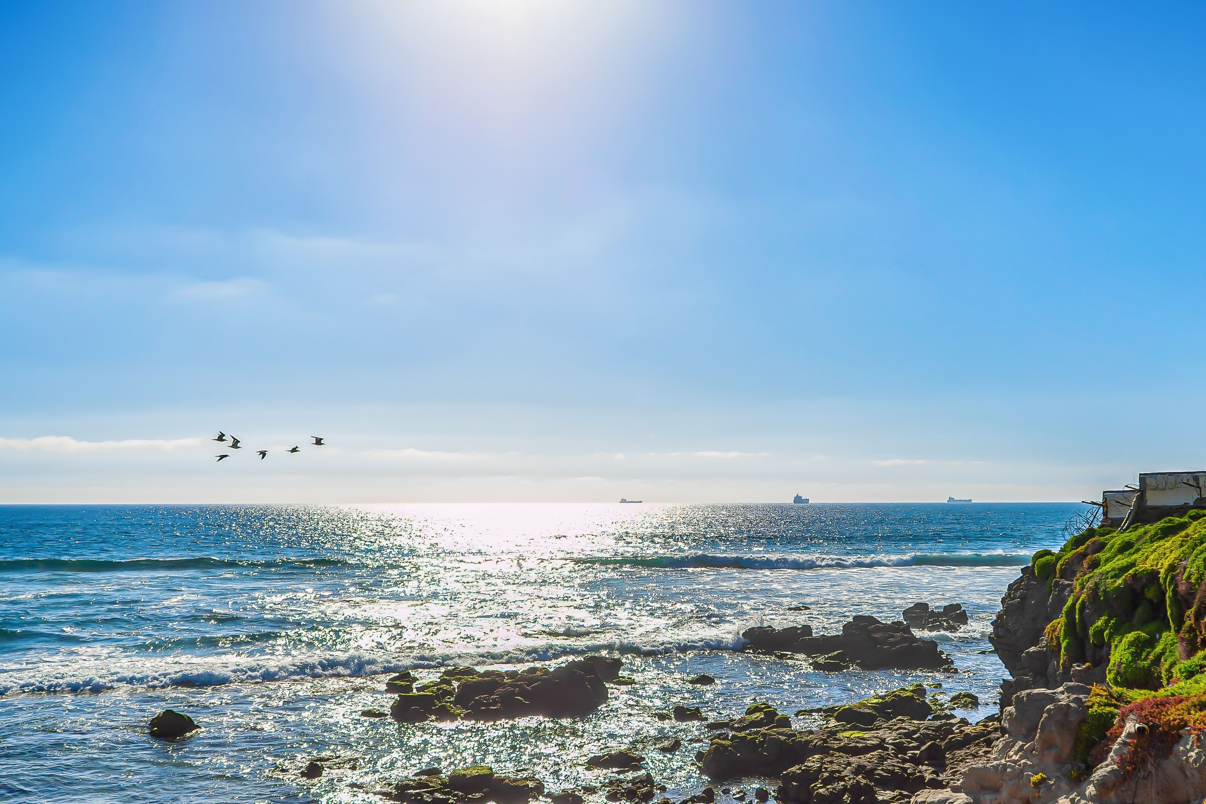 A coastal scene with rocky terrain, clear skies, and distant ships.