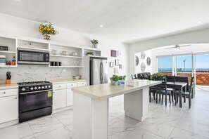 A modern kitchen with white cabinetry, a central island, and a dining area with a view. - Dog-friendly Home With Heated Pool, Hot Tub, Partial Ocean Views, & Balcony (Playas de Rosarito)