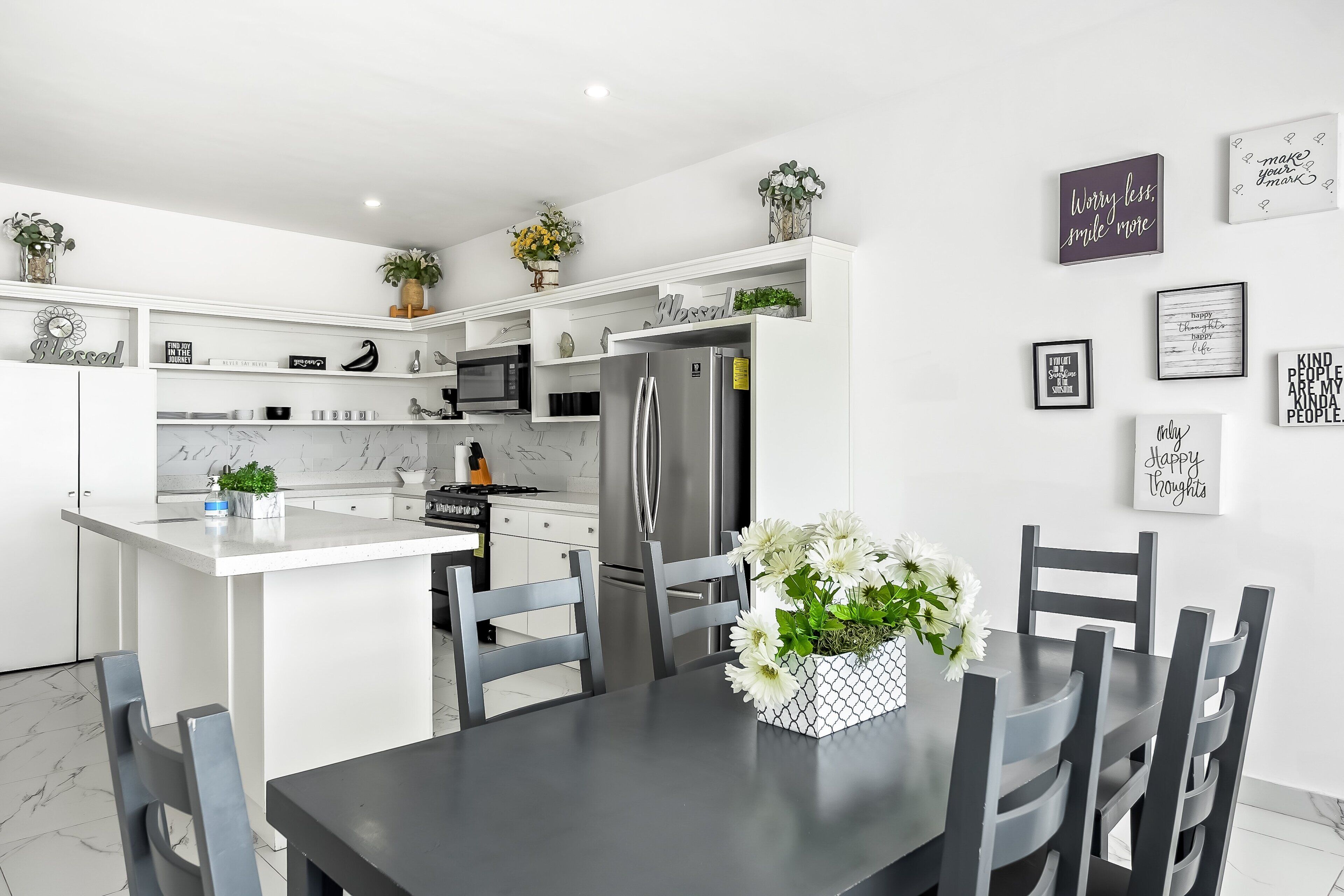 A modern kitchen with white cabinetry, a central island, and a dining area with a table and chairs.