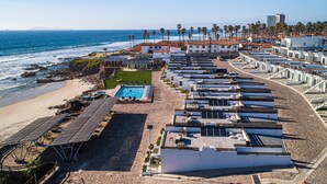 Um hotel à beira-mar com edifícios de vários andares, área de praia com piscina e vista para o oceano.