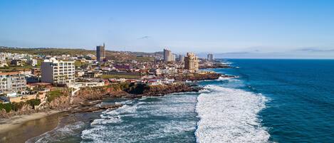 Un paysage urbain côtier avec des bâtiments le long de la côte, un ciel bleu dégagé et des vagues qui déferlent sur la plage.