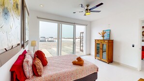 Um quarto com cama, ventilador de teto, armário de madeira e vista para o exterior.