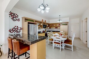 A modern kitchen with a central island, white dining set, and decorative wall art. - Dog-friendly Villa With Heated Outdoor Pool, Hot Tub, Streaming, Partial Views (Playas de Rosarito)
