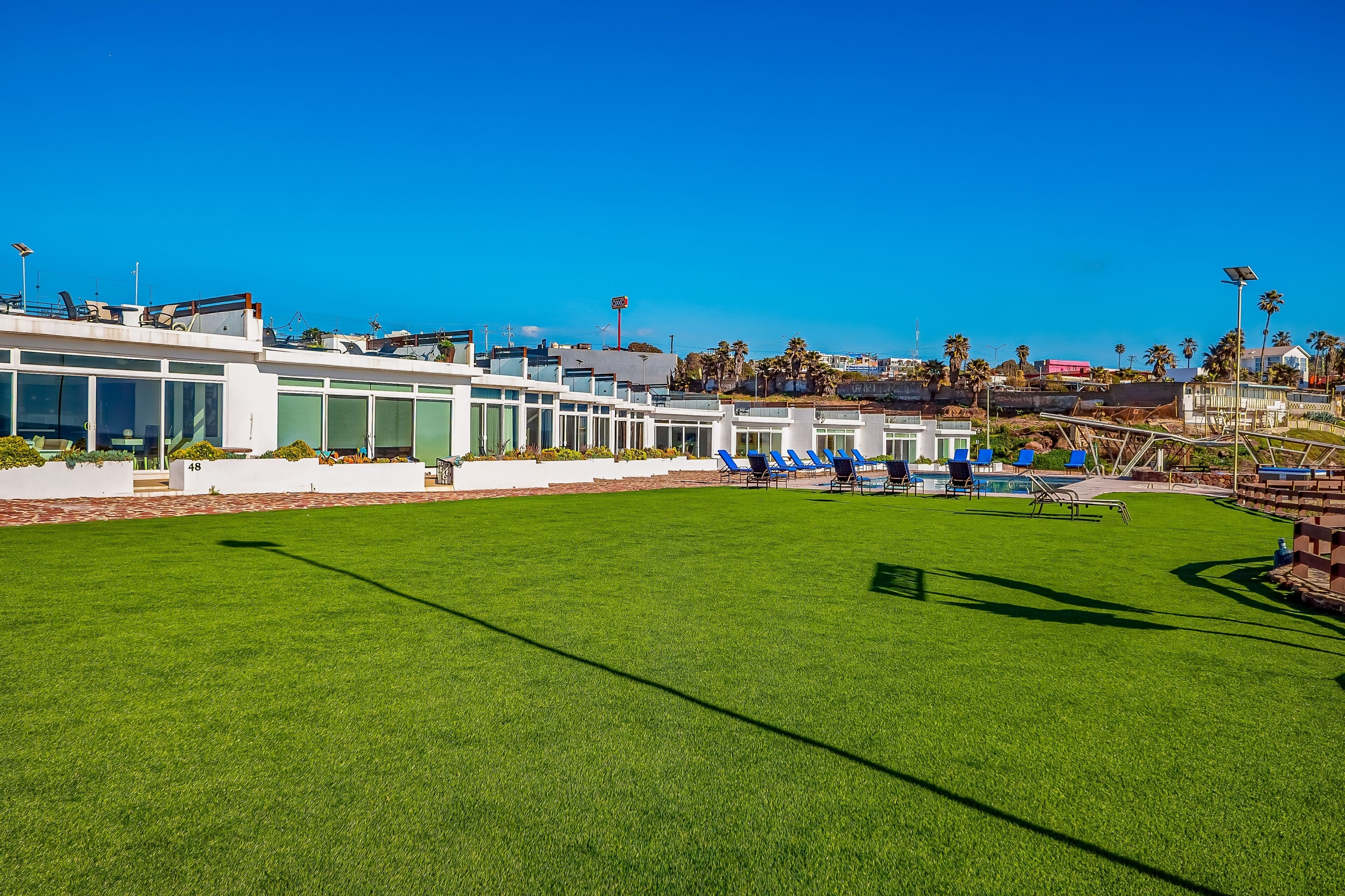 A hotel with a large outdoor pool area, a well-maintained lawn, and a row of blue chairs.