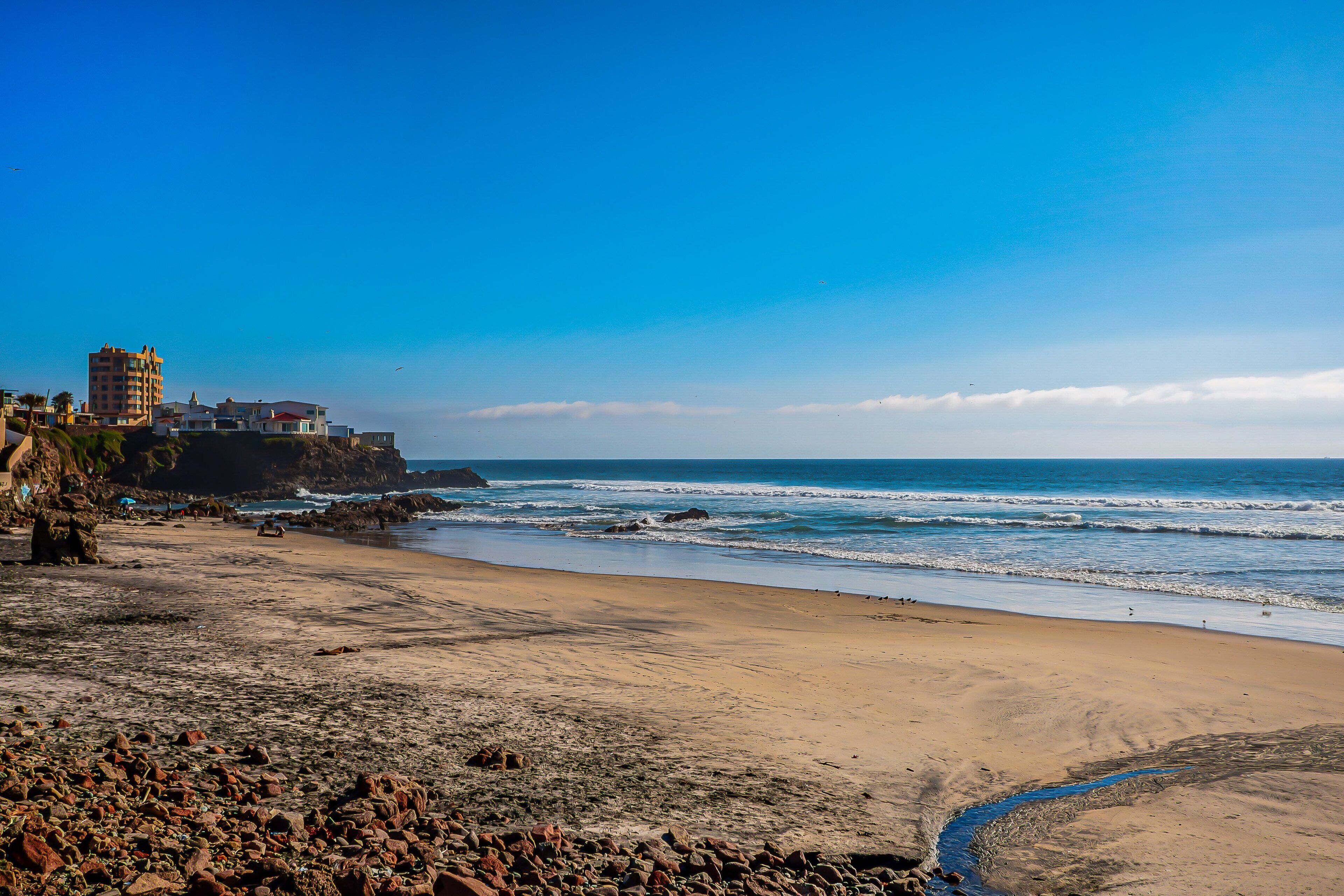 Una playa costera con terreno rocoso, un edificio en un acantilado y el océano.
