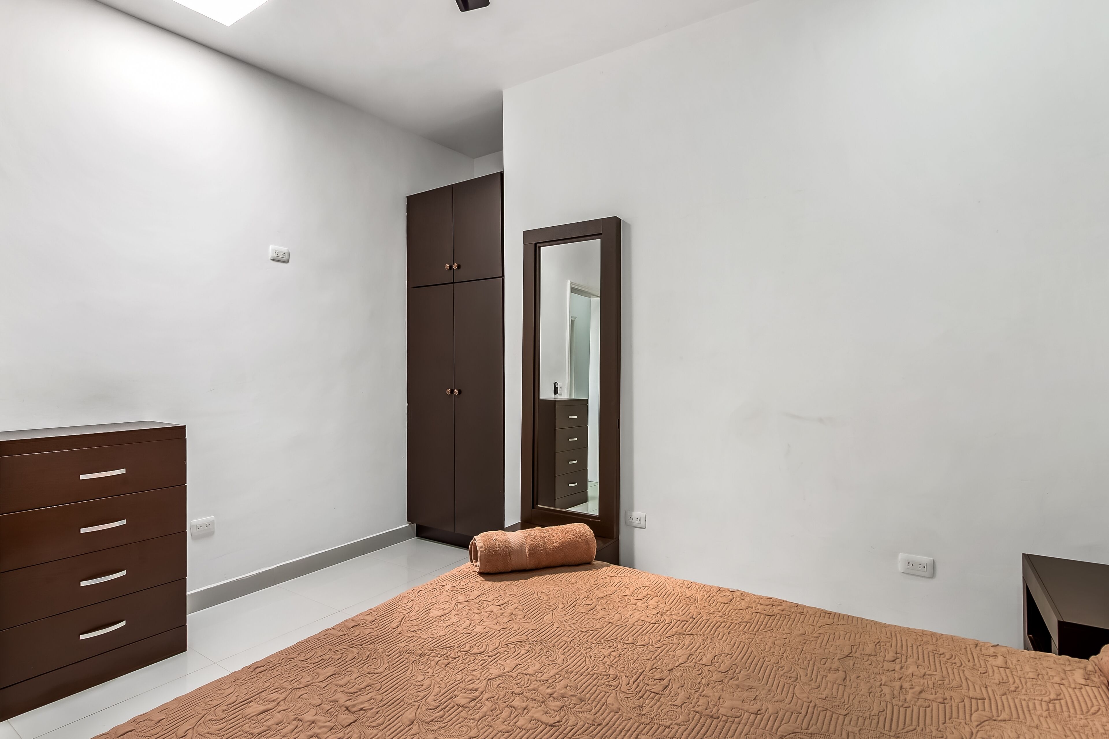 Un dormitorio con cama, armario, espejo y una pequeña mesa.