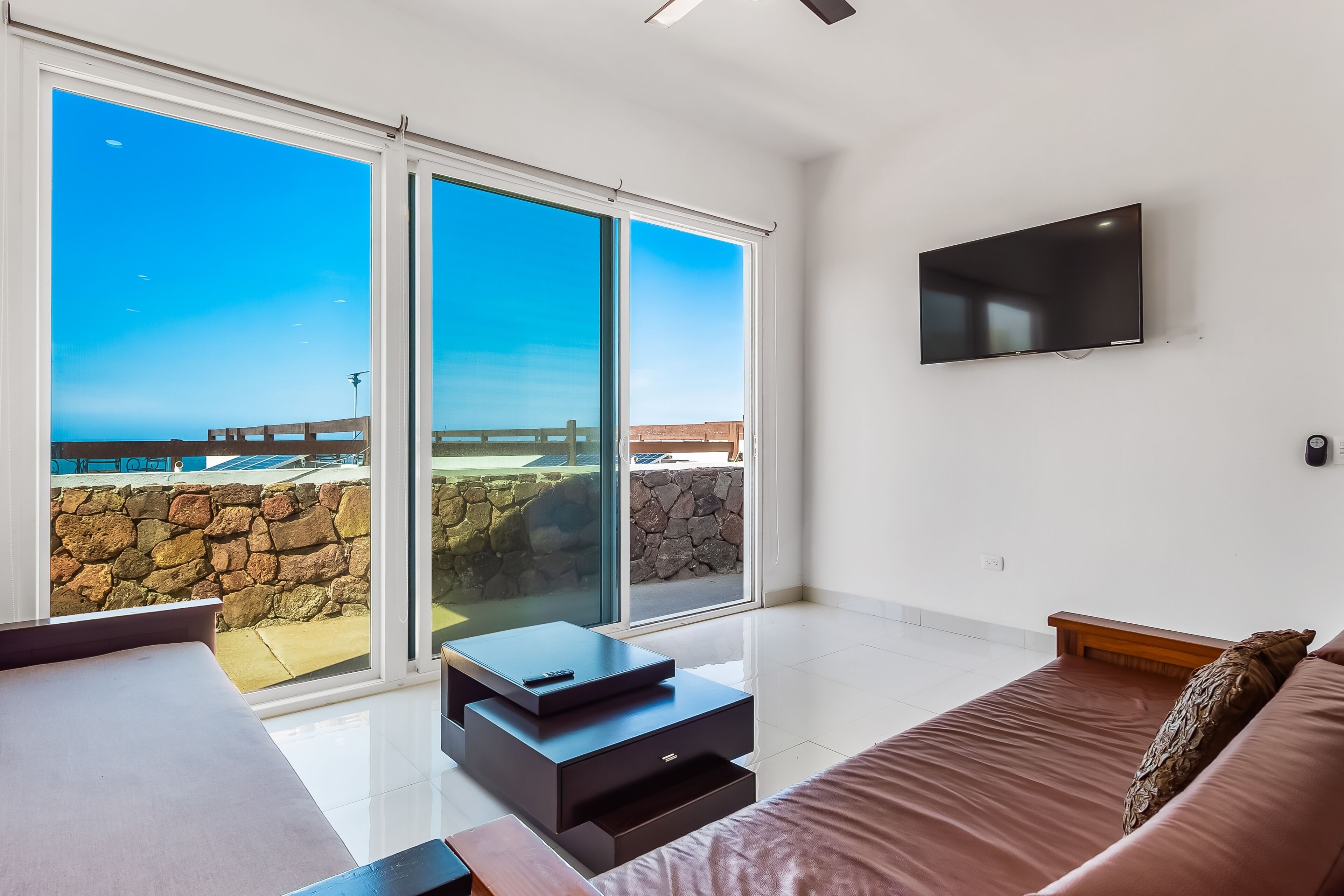 A modern bedroom with a large sliding glass door leading to a balcony with a stone wall and a wooden deck.