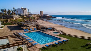 Área da piscina com cadeirões azuis, uma piscina pequena e vista para o oceano.