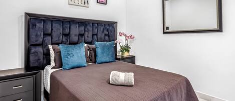 Ein modernes Schlafzimmer mit einem großen Bett, einem dunklen Kopfteil und dekorativen Kissen.