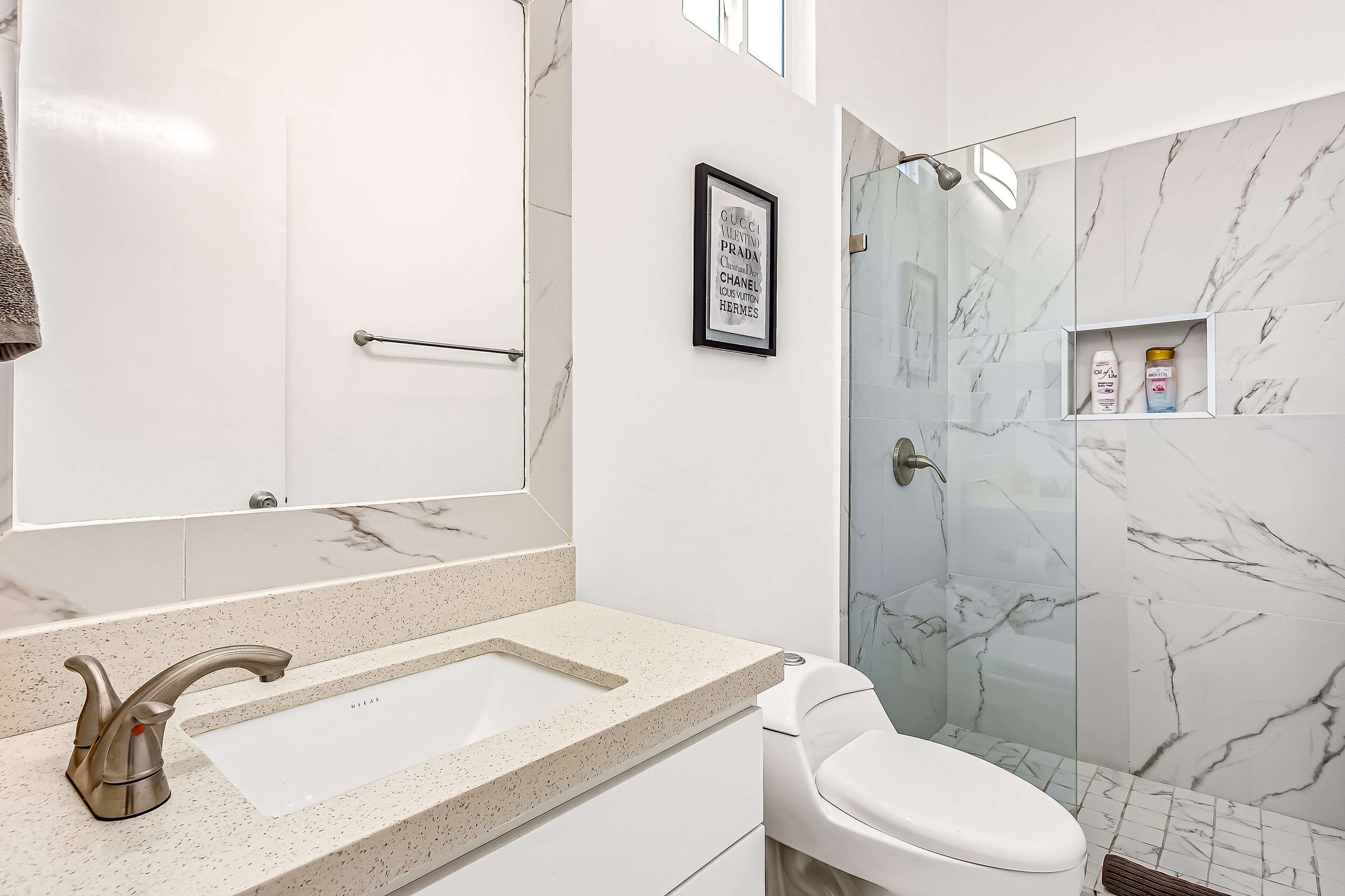 A bathroom with a marble sink, a toilet, a shower with glass doors, and a framed picture on the wall.