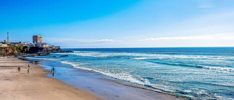 A beach with a clear sky, waves, and a few people walking.