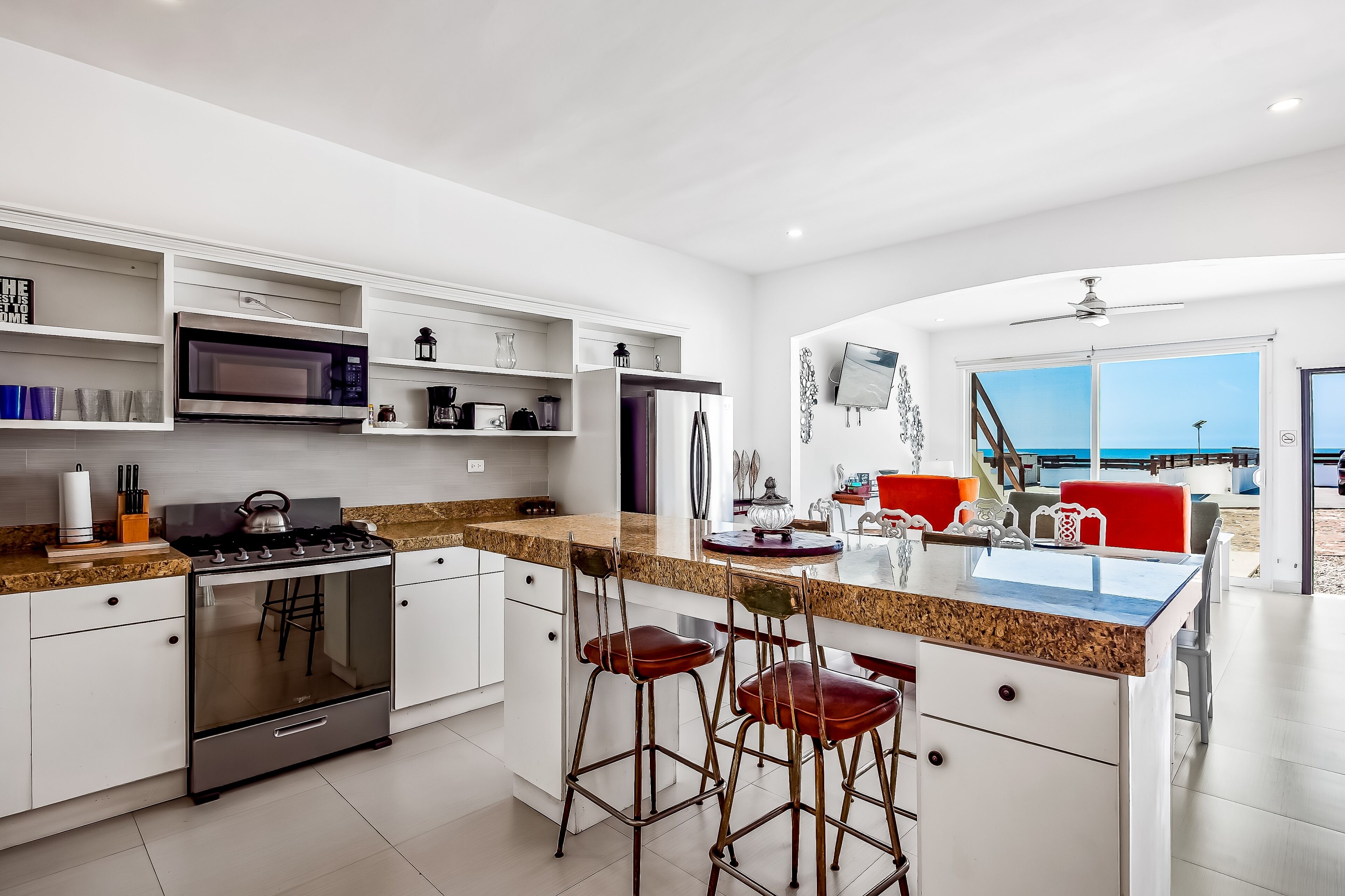 A modern kitchen with white cabinetry, a stainless steel stove, and a large island with bar stools.