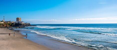 A beach with a clear sky, waves, and a few people walking.