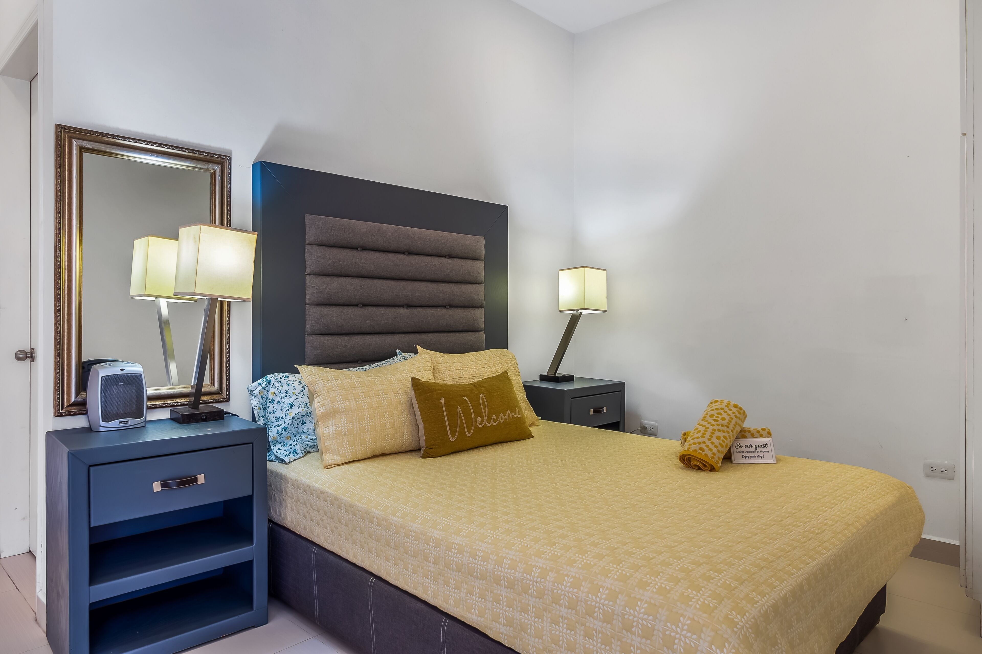 Un dormitorio ordenado con cama, mesitas de noche, un espejo y una lámpara de noche.