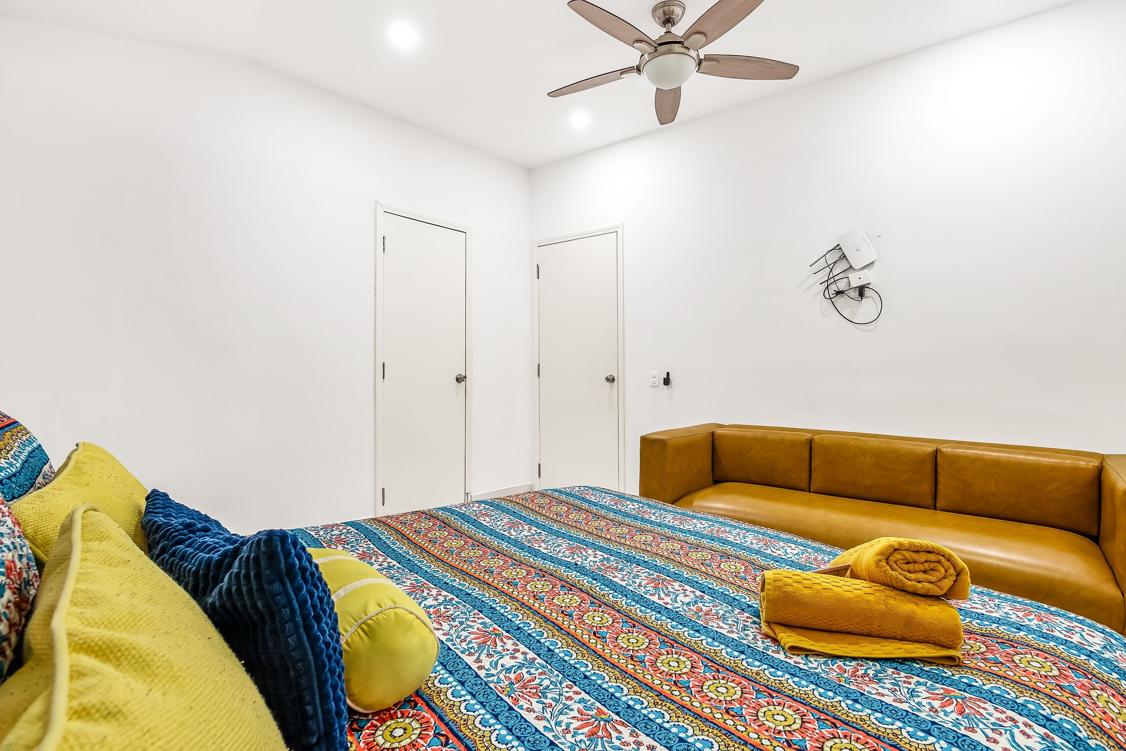Un dormitorio con cama, ventilador de techo y lámpara en la pared.