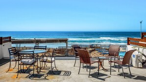 Una terrazza con posti a sedere all'aperto, vista sull'oceano e una spiaggia sullo sfondo.