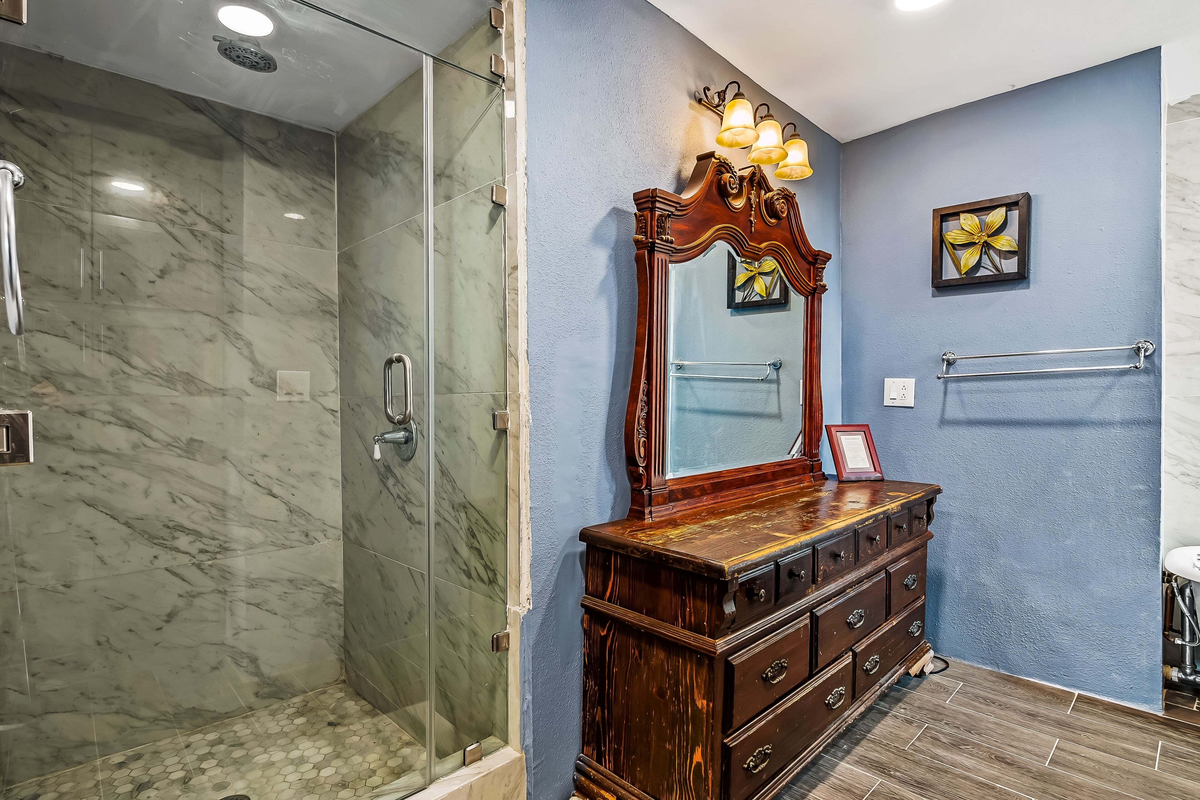 A bathroom with a glass-enclosed shower, a wooden vanity with drawers, a large mirror, and a towel rack.