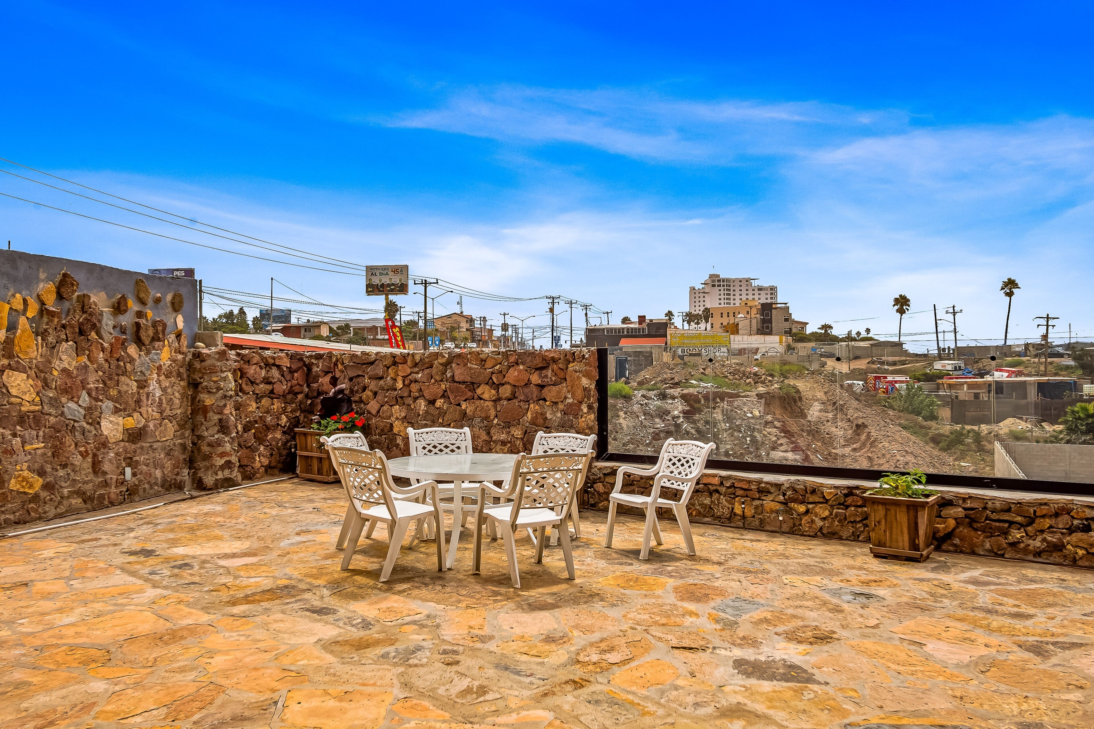 An outdoor patio with stone flooring, white chairs, and a table.