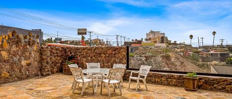 An outdoor patio with stone flooring, white chairs, and a table.