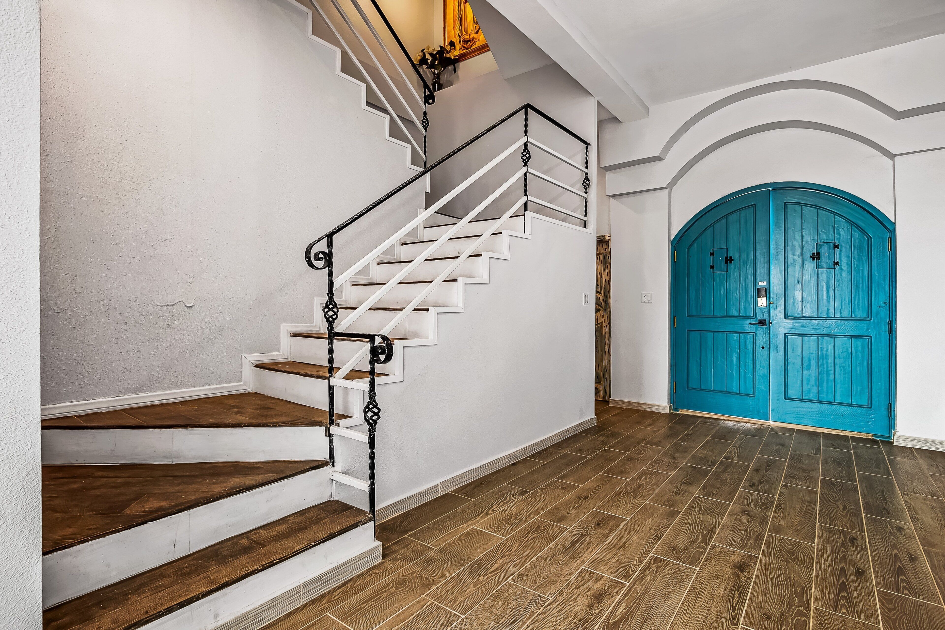 Una escala amb baranes blanques i graons de fusta que condueix a una porta color turquesa.