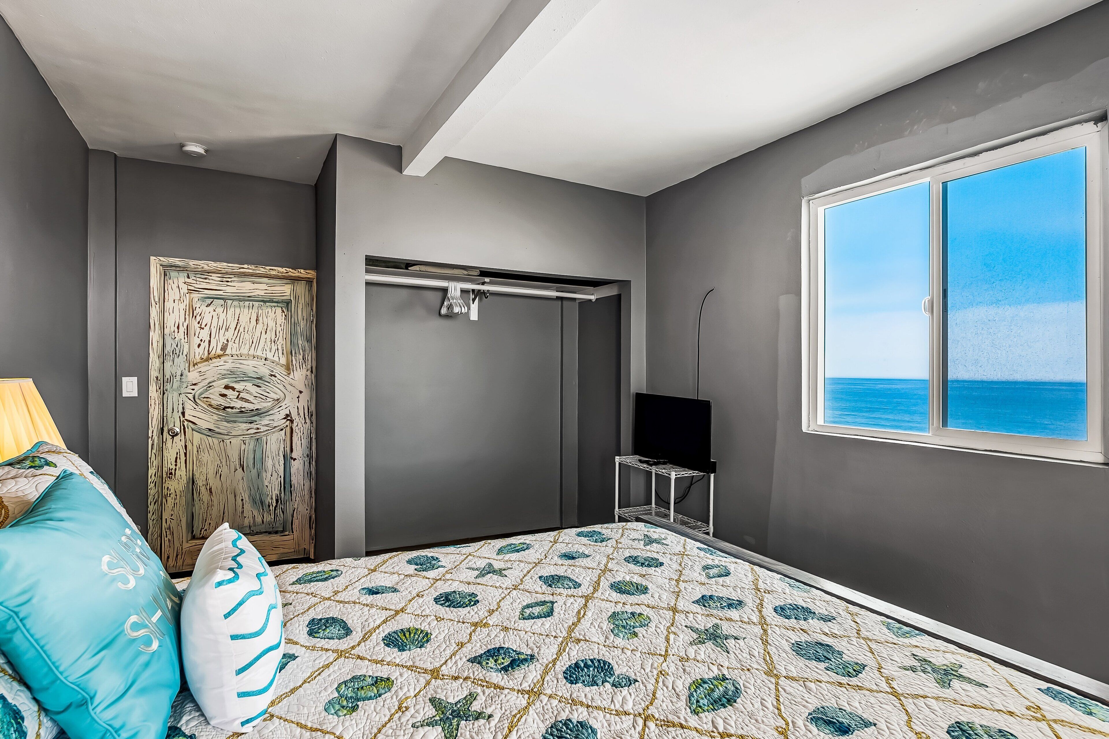 A bedroom with a bed, a TV, a window with a view, a door, and a ceiling light.