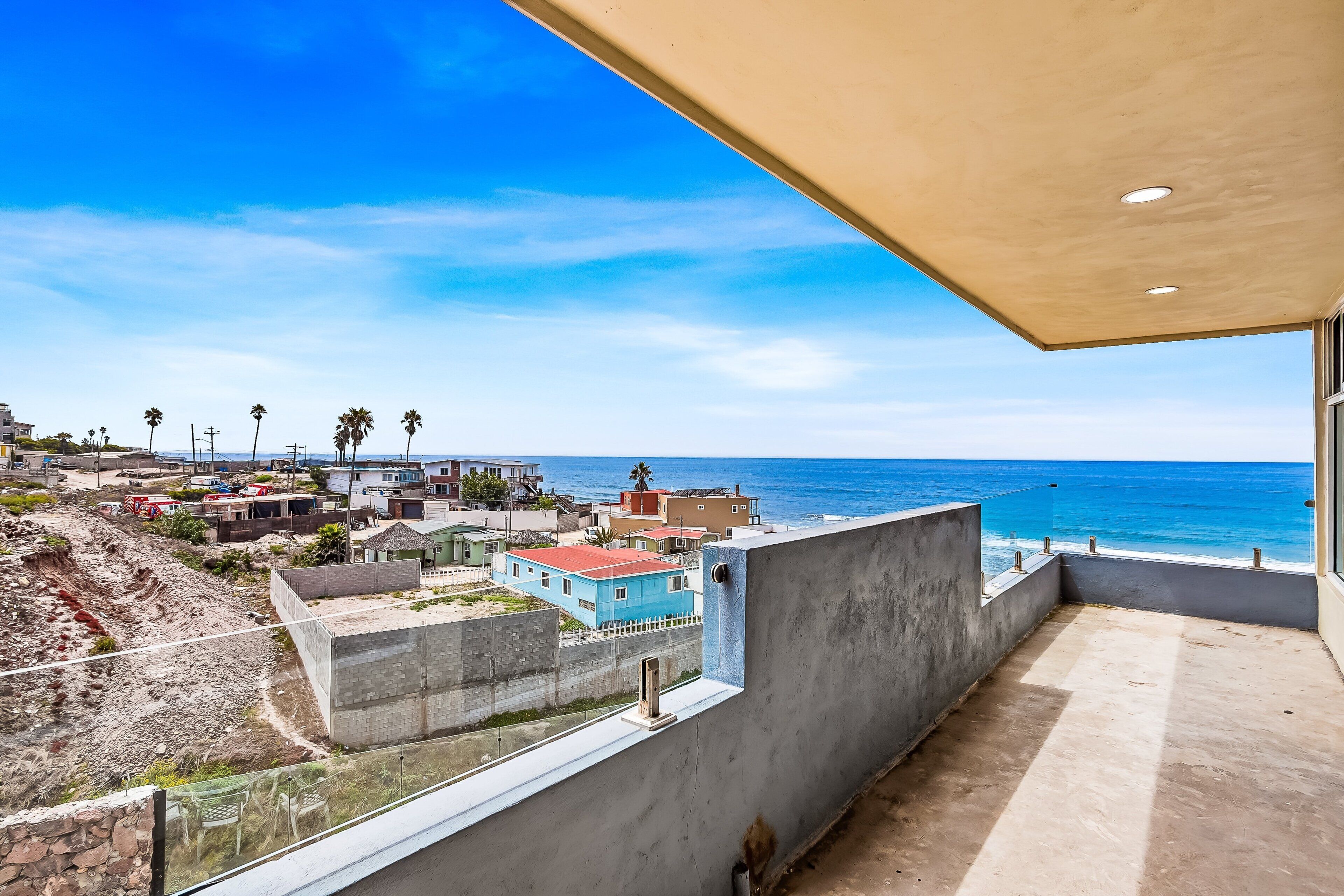 A balcony with a view of the ocean, a concrete wall, and a building with a red roof.