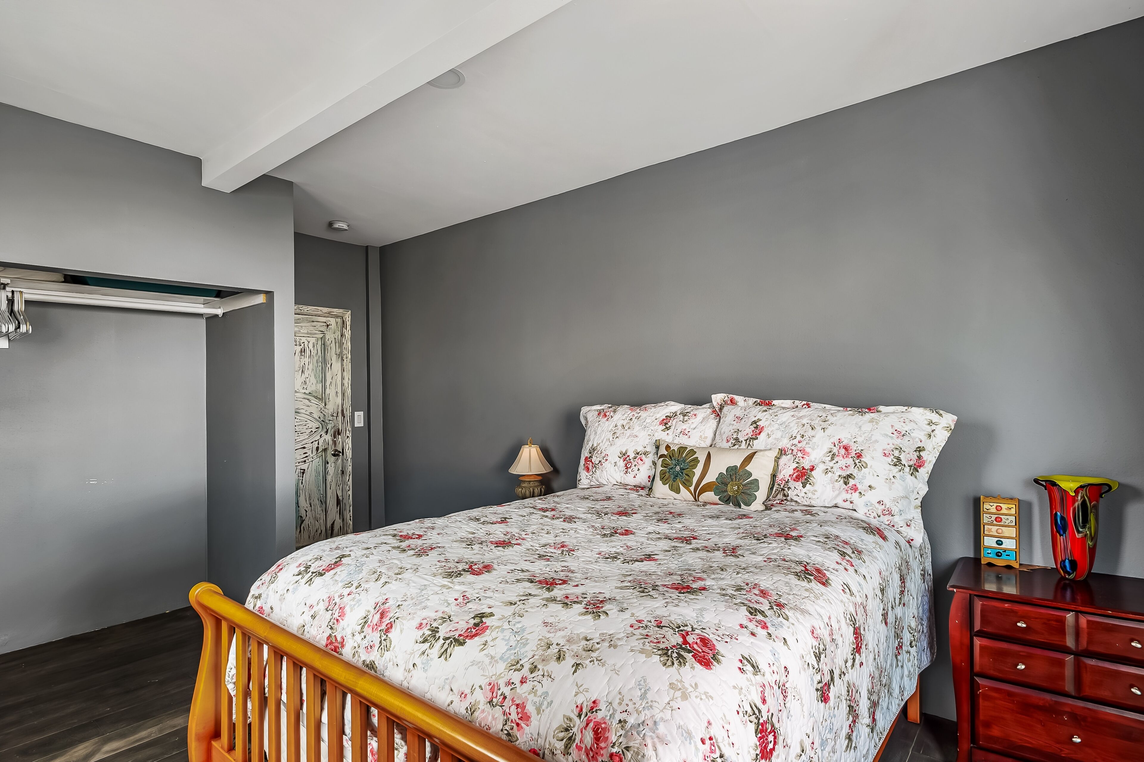 Une chambre à coucher avec un lit, une tête de lit en bois, une table de chevet avec une lampe, une commode et un vase.