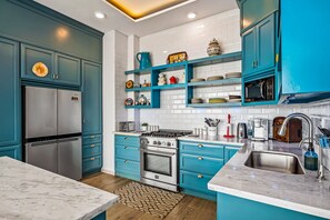 Une cuisine moderne avec des armoires de couleur turquoise, des appareils en acier inoxydable et un comptoir en marbre.