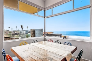 Un comedor con mesa de madera y sillas coloridas, con vistas a una playa y al océano.