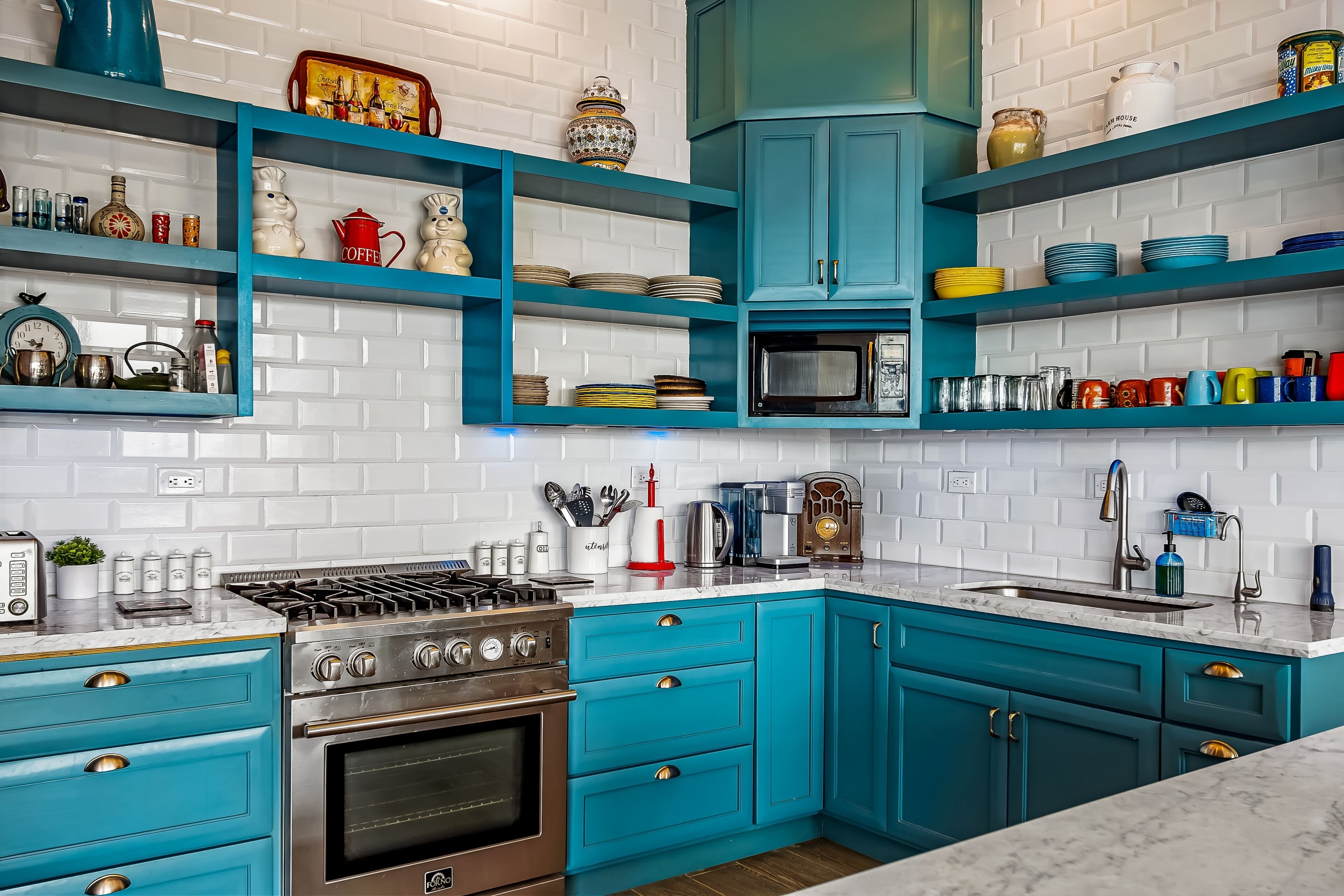 A kitchen with teal cabinets, a stove, and various kitchen items on shelves.