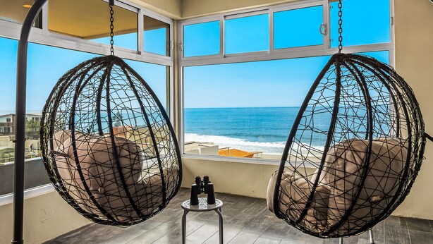 Two hanging chairs with a view of the ocean through large windows. - Tropical Retreat With Ocean Views - Steps From the Sand With Alfresco Dining (Playas de Rosarito)