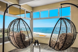 Une pièce dotée de deux fauteuils suspendus, placés face à une grande fenêtre donnant sur l’océan.
